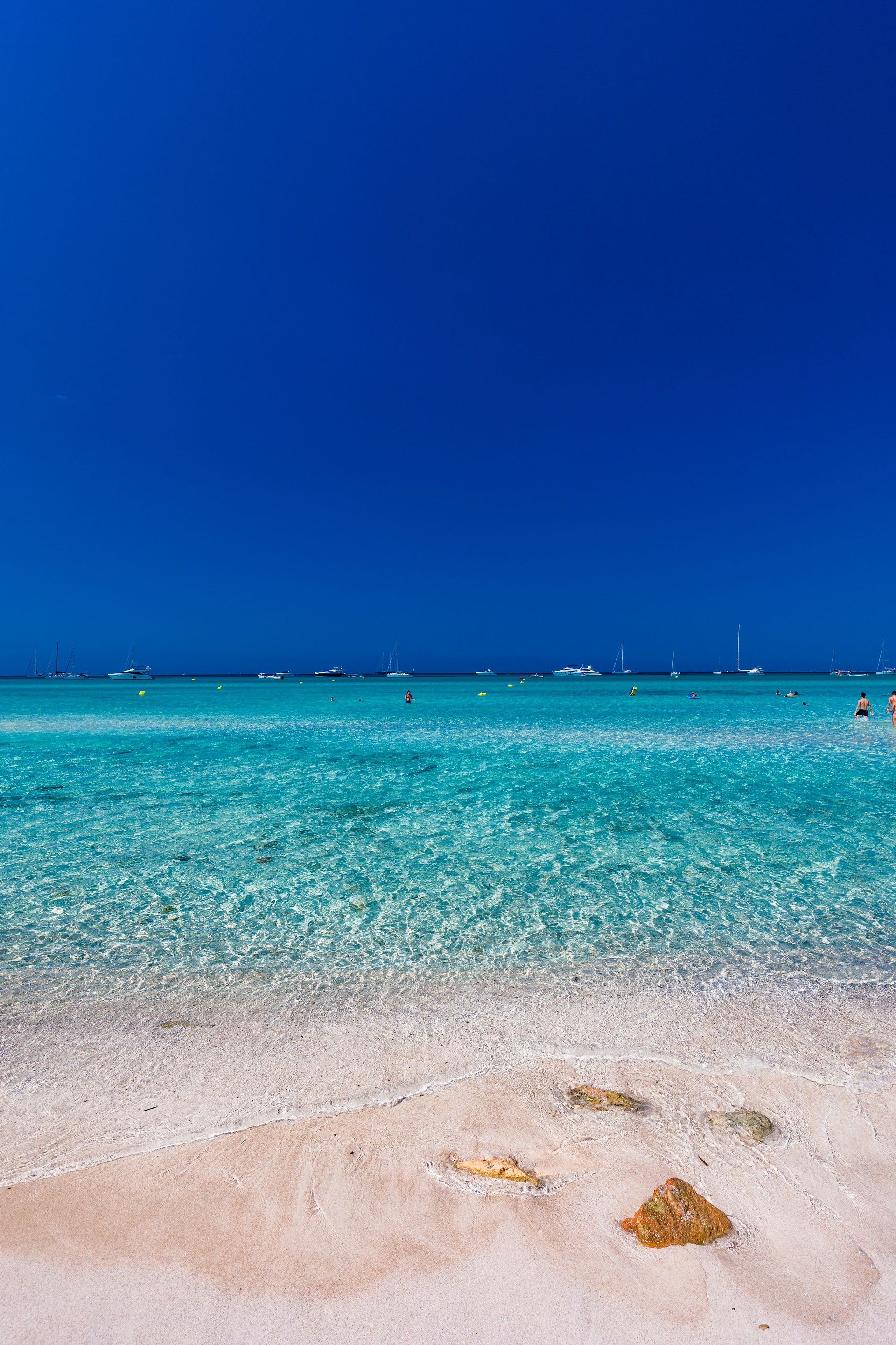 Strand auf Mallorca mit türkisblauem Wasser, feinem Sand und grünen Hügeln im Hintergrund unter blauem Himmel.