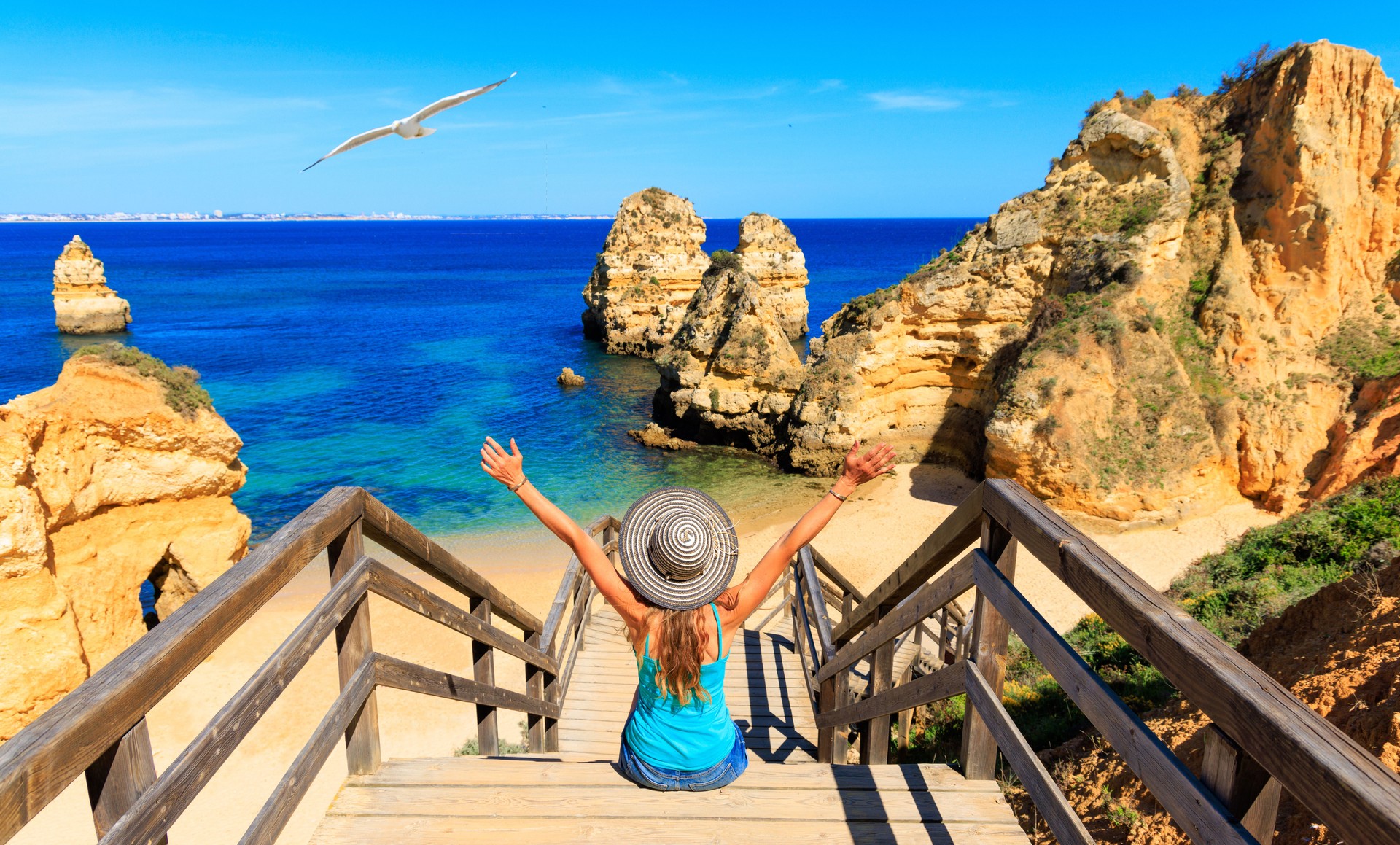 Glückliche Touristin sitzt auf der Fußgängerbrücke zum schönen Strand Praia do Camilio, Ponta da Piedade - Algarve Strand, Tourismus in Portugal